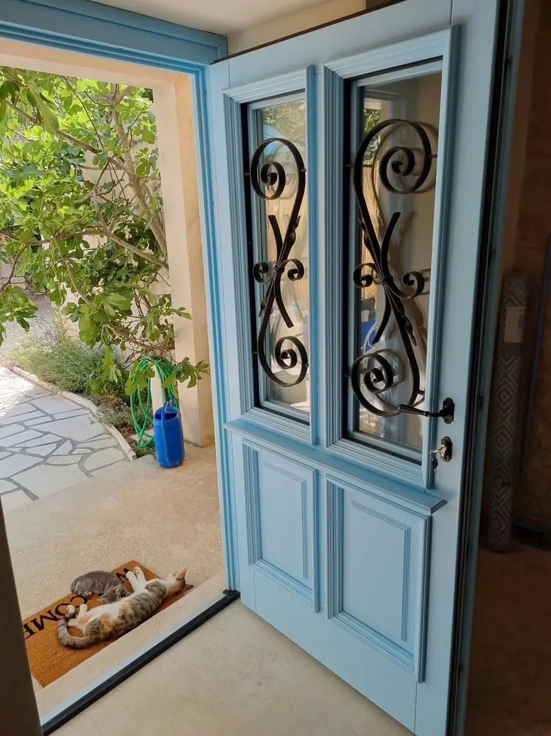 Hellblaue Eingangstür von Casa Bella mit schmiedeeisernem Gitter, draußen Feigenbaum und gepflasterter Weg