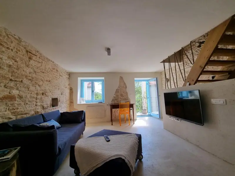 Wohnzimmer im 1. Stock mit Natursteinwand, Sofa, Fernseher und offener Holztreppe