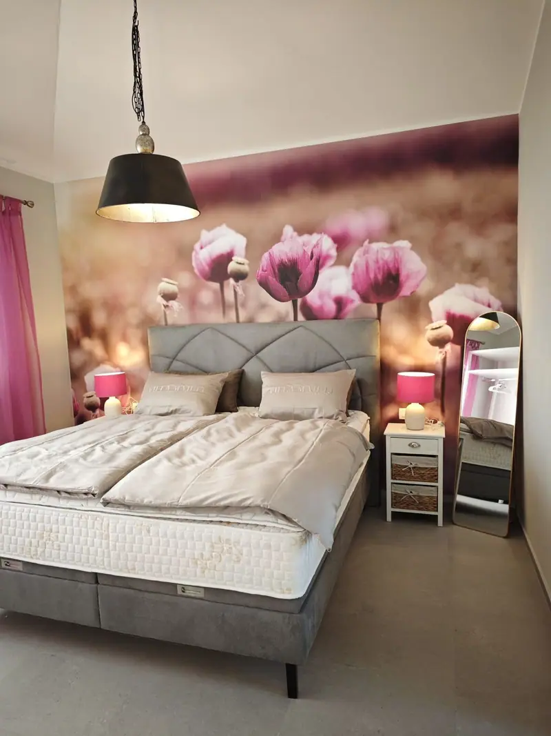 Bedroom with box spring bed in front of poppy wallpaper