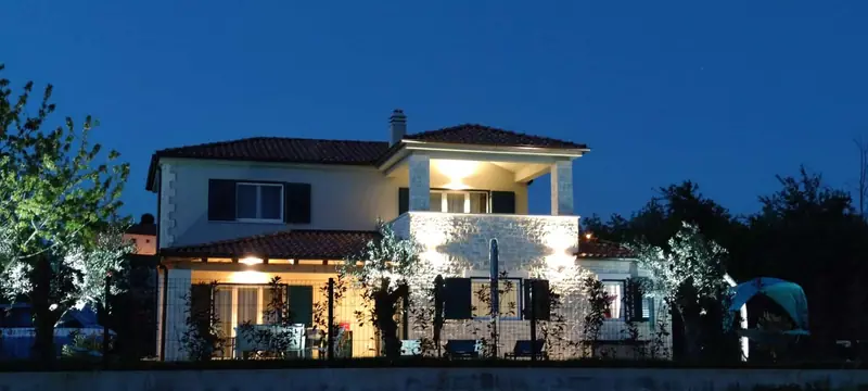 The house lit up in the evening, with olive trees in the garden