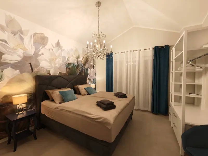 Bedroom with box spring bed, lotus flower wallpaper and blue curtains